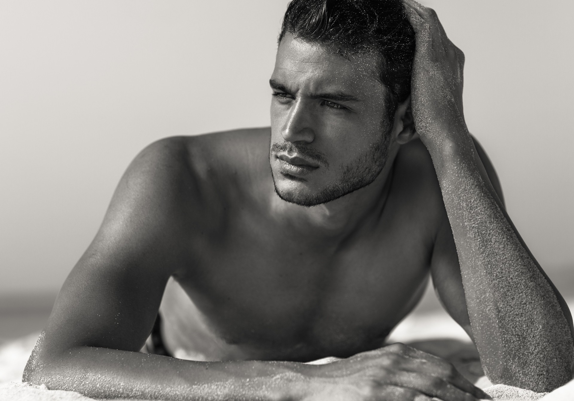 Handsome sexy shirtless male model lying on the sand at the beach. Beauty portrait.