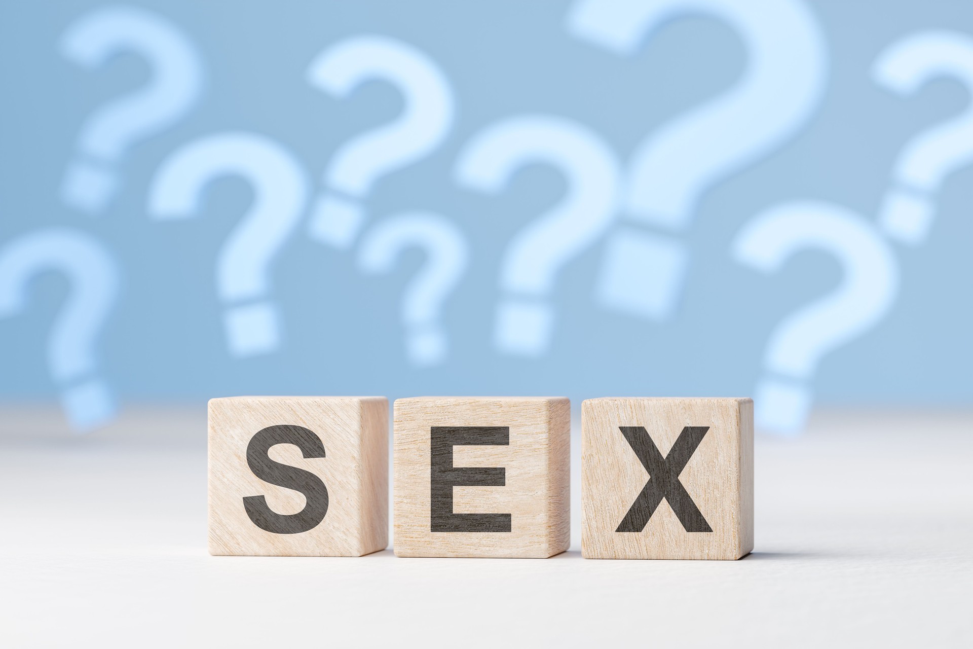 Sex question. Word sex is laid out with wooden cubes on background of many question marks.