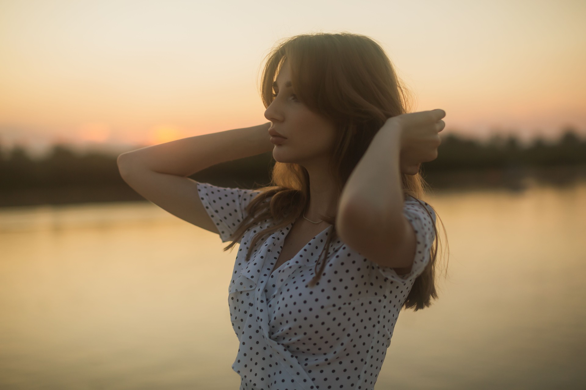 Young woman enjoying sunset on the river bank. Summer evening