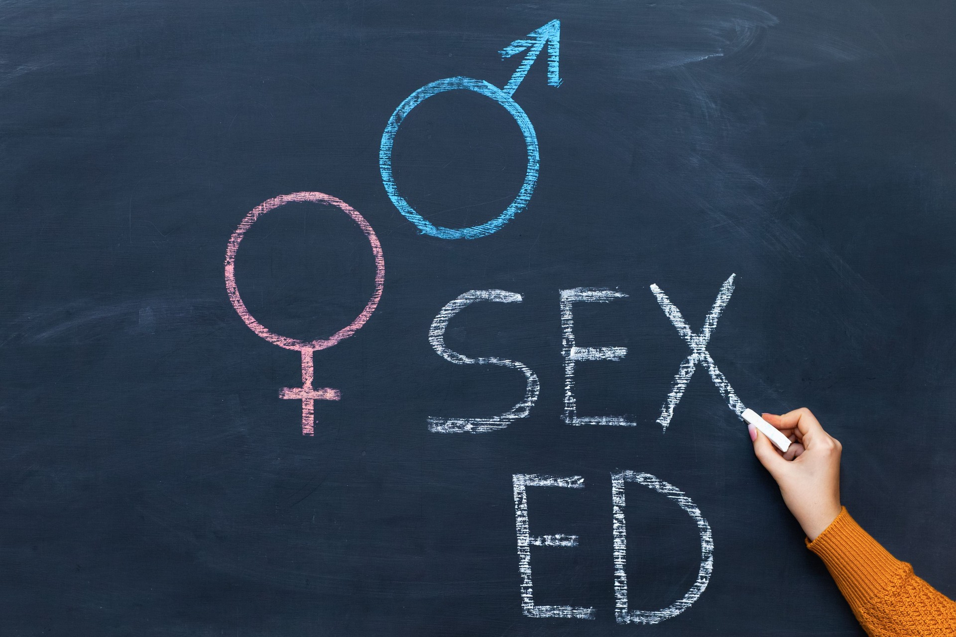 Gender symbols of a man and a woman on a chalkboard, a woman's hand writes the text SEX ED